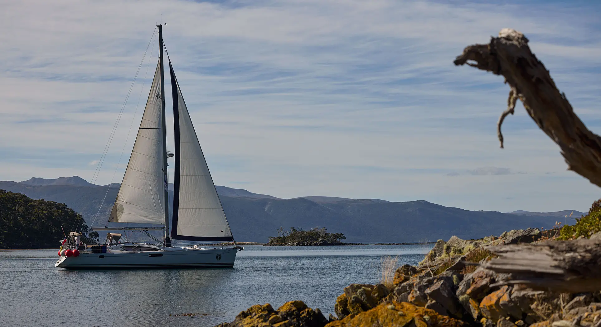 A white sailing yacht with sails set glides through a calm bay