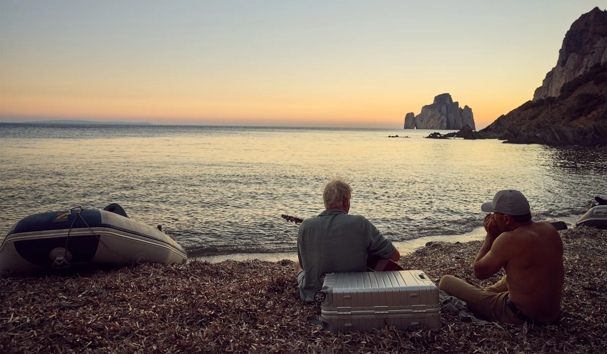 Two men sitting on pebble beach with guitar