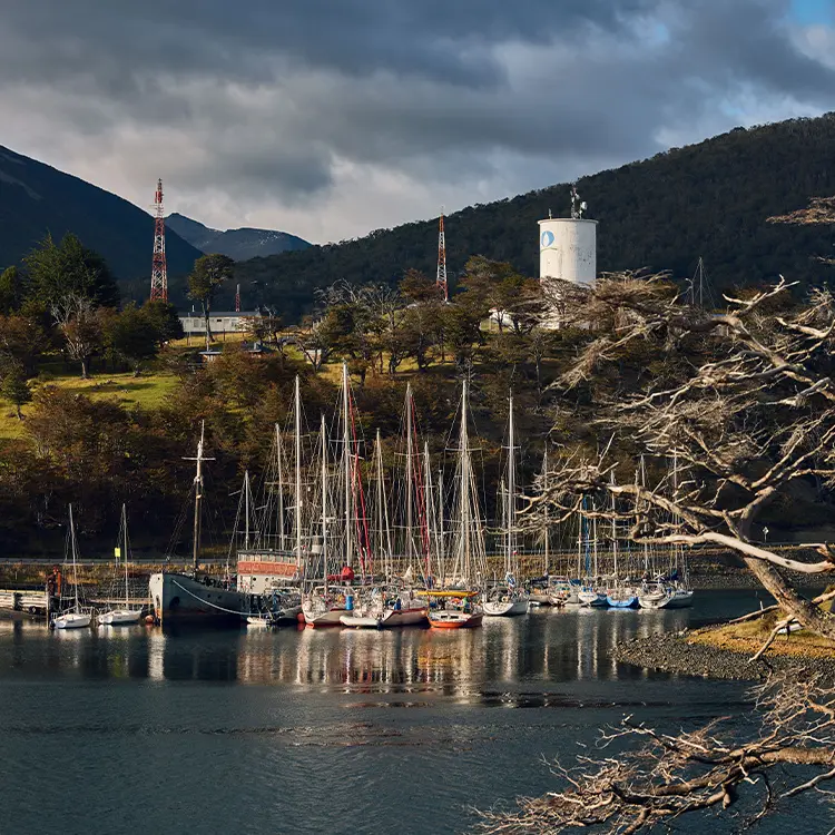 Sailing boats lie in a small harbour in front of wooded hills
