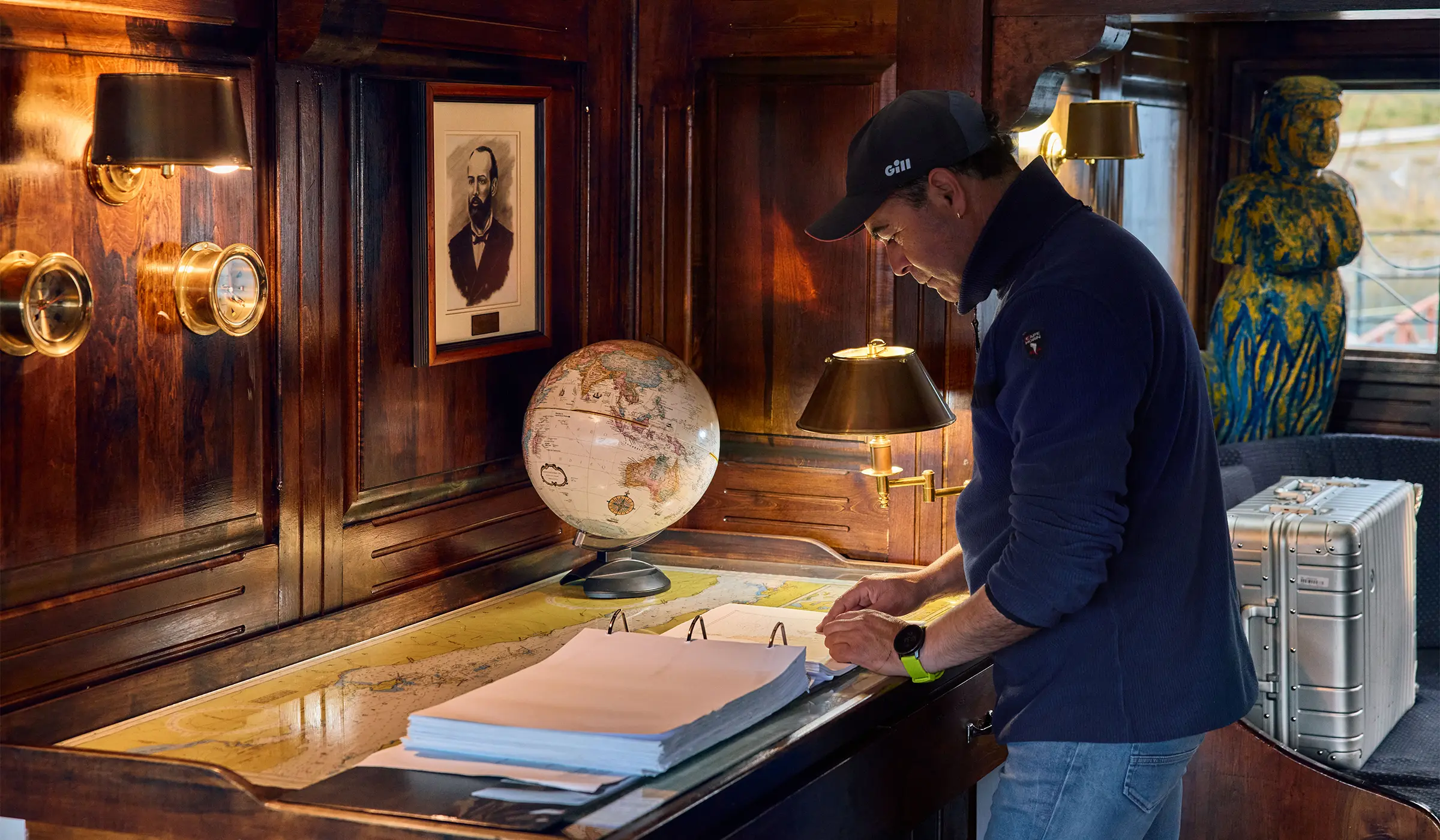 A man studies nautical charts in a wooden ship’s cabin