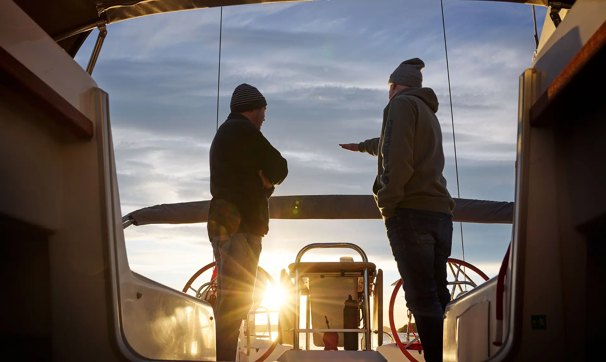 Two people stand at sunset at the helm of a sailing yacht