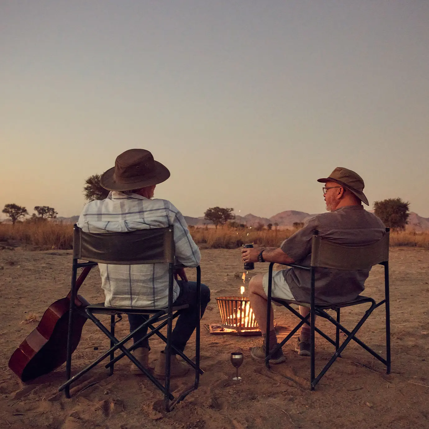Two men on camping chair in front of fire basket