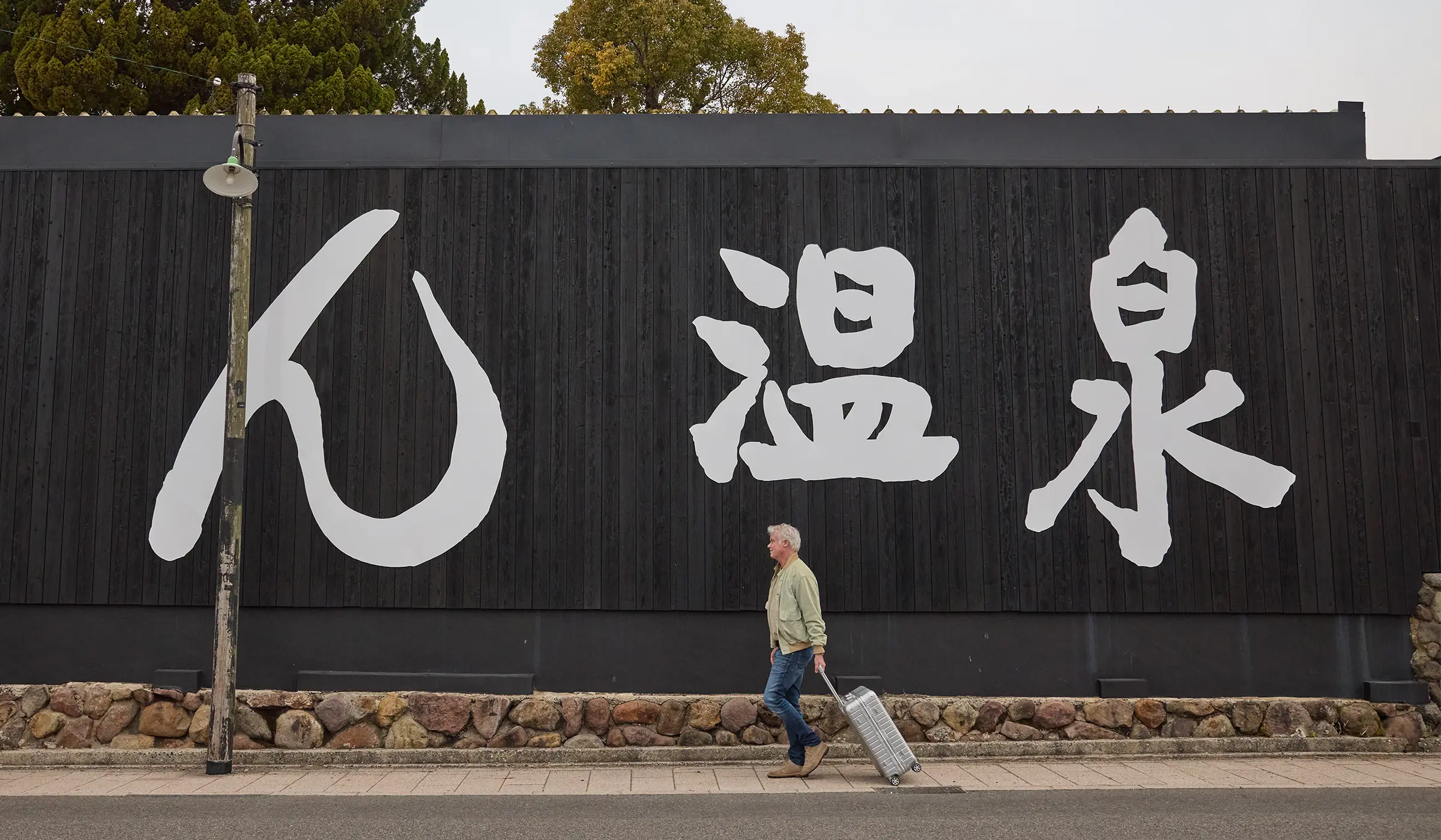 Man pulling an aluminium suitcase past onsen lettering on a house wall – typical scene among Japan’s tourist sights